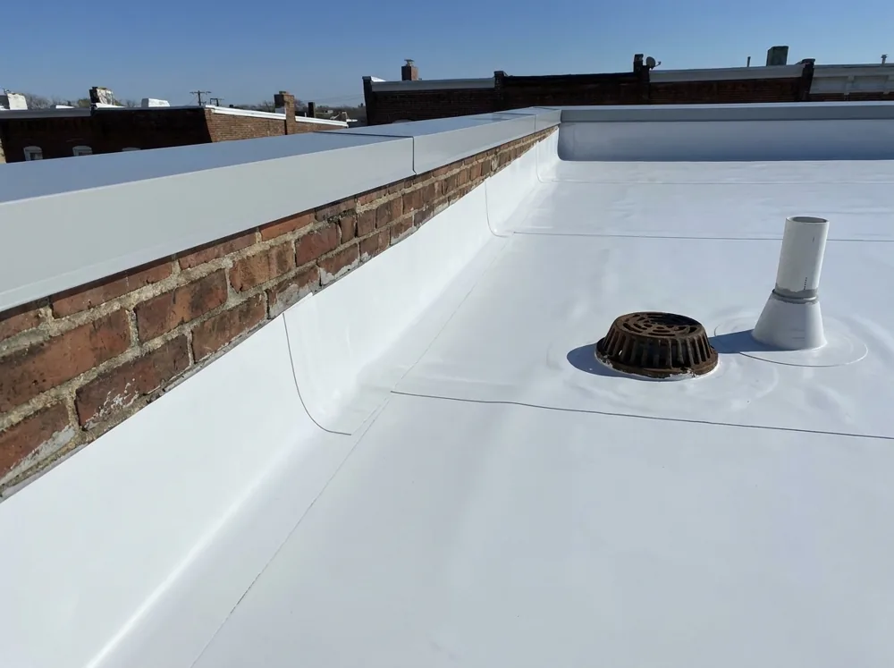 New white TPO single-ply membrane installed on a Baltimore rowhouse flat roof with welded seams and a fresh metal coping cap on the brick parapet