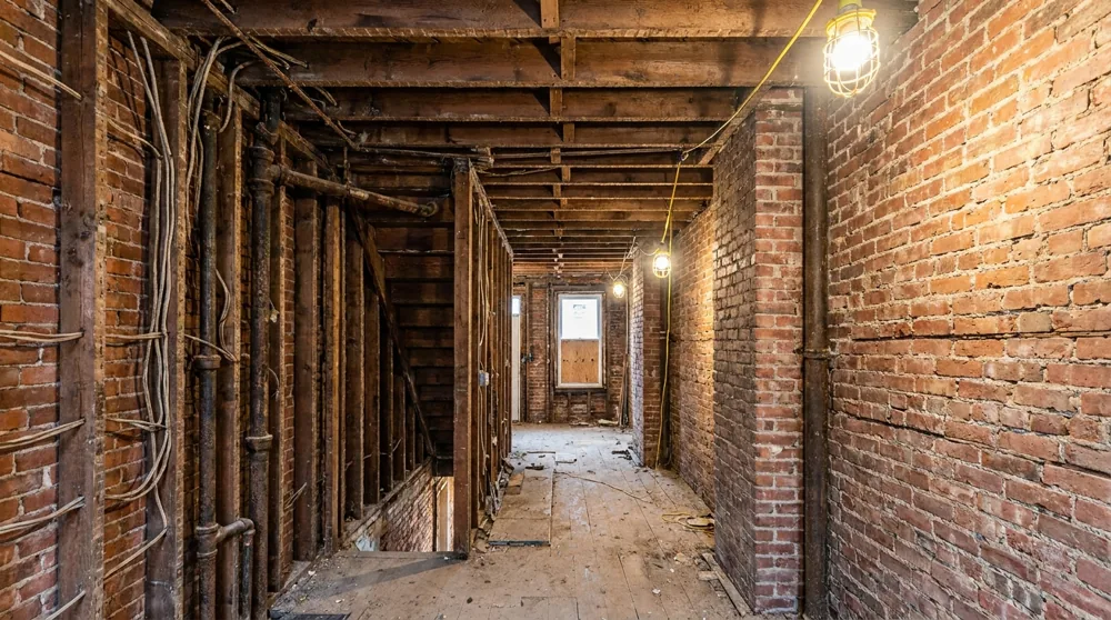 Exposed floor joists, brick party walls, and old wiring inside a Baltimore rowhome stripped to the studs during renovation