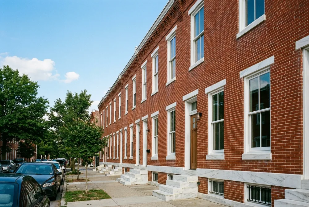 A row of Baltimore brick rowhouses with new white double-hung replacement windows and marble steps