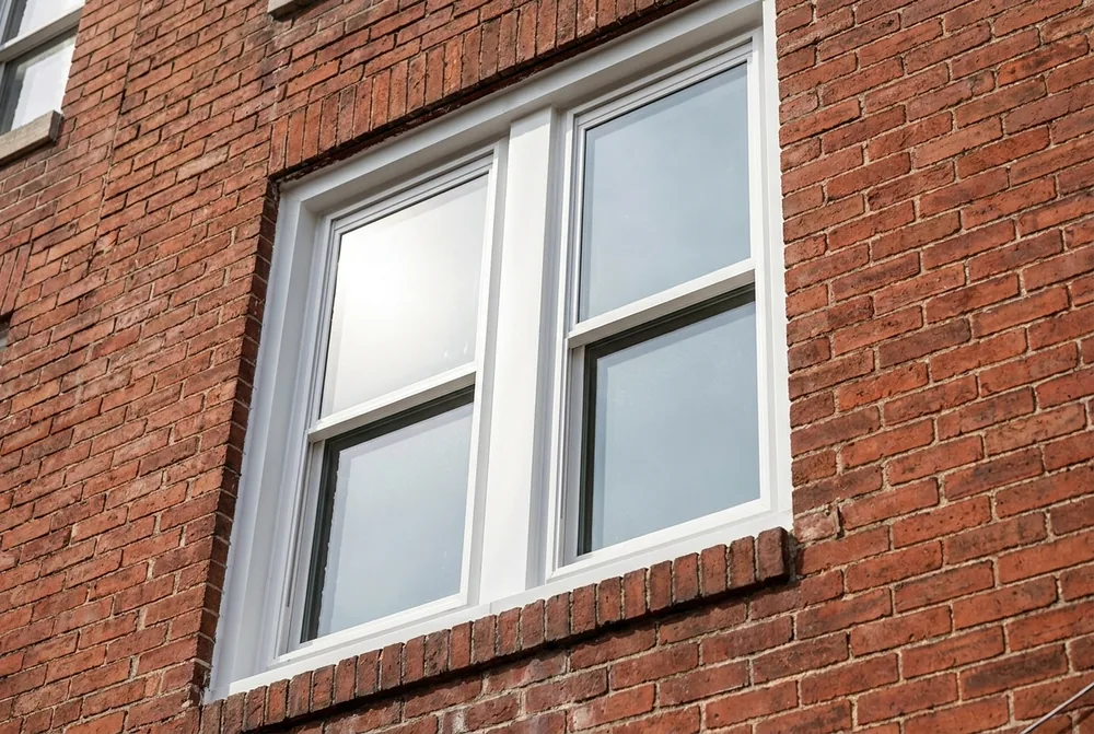 New white double-hung replacement window set into a Baltimore red brick rowhouse facade